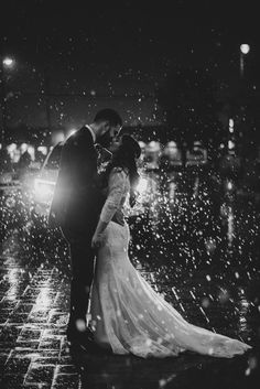 a bride and groom standing in the rain at night with their arms around each other