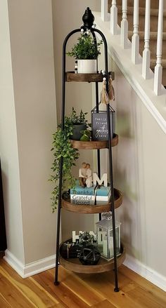 a three tiered shelf with books and plants on it in front of a stair case