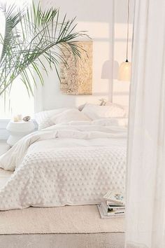 a bed with white sheets and pillows next to a potted plant on top of it