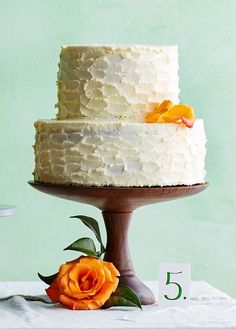 a three tiered cake with white frosting and an orange flower sits on a wooden stand