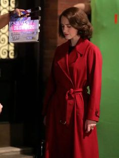 a woman in a red coat standing next to a green wall with a sign on it