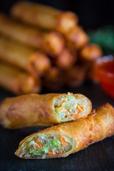 two vegetable spring rolls on a table with some dipping sauces in the back ground