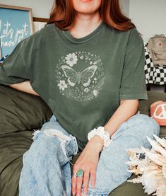 In this wildflower butterfly tee, a graceful silhouette flutters amidst a vibrant arrangement of blooms, inviting you to immerse yourself in nature's beauty. Let this charming design elevate your spirit with every wear. ★ Fabric ★ The Comfort Colors 1717 tee is made with medium fabric (6.1 oz/yd² (206.8 g/m consisting of high quality, 100% ring-spun US cotton for long-lasting comfort. Made using 100% US cotton that is ethically grown and harvested. ★ Fit ★ The relaxed fit keeps the wearer comfy in both casual and semi-formal settings while the crew neckline delivers that classic, neat style which makes it perfect for accessorizing.  The pre-shrunk fabric ensures a consistently great fit. ★ Care Instructions ★ ● Machine wash at a low heat. ● Wash garments inside-out, with similar colours. ● Casual Printed Tops With Butterfly Sleeves, Casual Green Top With Butterfly Print, Summer Fairycore Top With Graphic Print, Spring Fairycore Cotton Tops, Fairycore Short Sleeve Tops For Spring, Butterfly Print Short Sleeve Tops For Spring, Green Butterfly Sleeve Tops For Spring, Short Sleeve Tops With Butterfly Print For Spring, Cotton Tops With Floral Print And Butterfly Sleeves