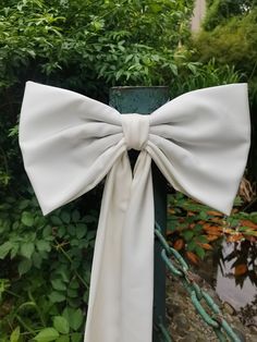 a white bow tied to a green pole in front of some bushes and trees,