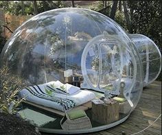 an inflatable bubble tent is sitting on a wooden deck with pillows and blankets