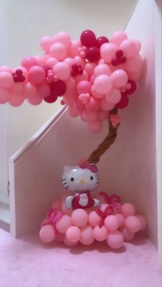 a hello kitty balloon tree with pink and red balloons on it's head, in front of a staircase