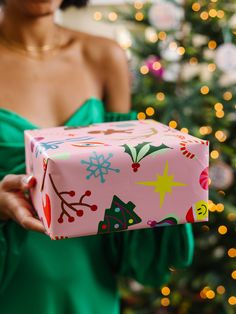 a woman in a green dress holding a pink present box with christmas decorations on it