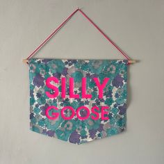 a sign hanging on the wall that says silly gooe in pink and blue flowers