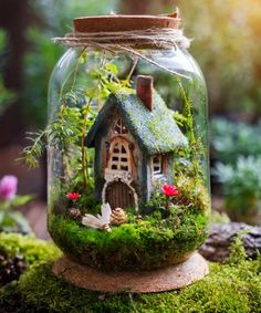 a glass jar filled with green moss and a small house in the middle of it