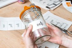 a person is holding a jar with the word cats written on it and scissors next to it