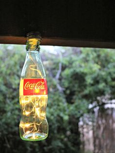 a bottle filled with light sitting on top of a window sill next to trees