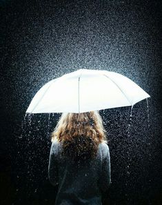 a woman standing under an umbrella in the rain with it's light shining on her