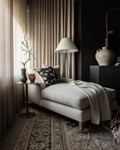 a white couch sitting next to a lamp on top of a wooden table in front of a window