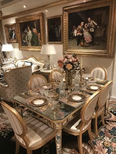 a fancy dining room set up with flowers on the table and paintings in the background