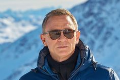 a man with sunglasses on standing in front of snow covered mountains and looking off into the distance