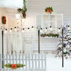 a white picket fence covered in snow next to a christmas tree