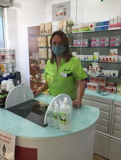 a woman wearing a face mask standing behind a counter in a store with lots of products on it