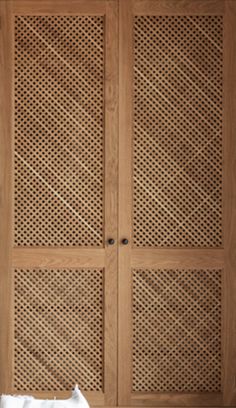 a white cat sitting on top of a bed next to a wooden closet with latticed doors