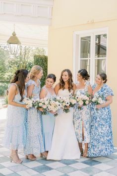 a group of women standing next to each other in front of a yellow building holding bouquets