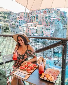 a woman sitting at a table with pizza and drinks on it in front of a cityscape