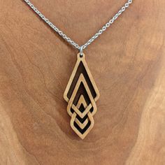 a wooden necklace with an intricate design hanging from a chain on a piece of wood