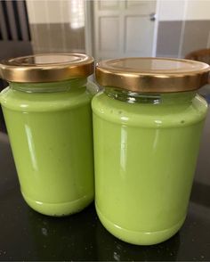 two green jars with gold lids sitting on a black counter top next to each other