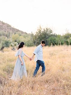 a man and woman holding hands walking through tall grass