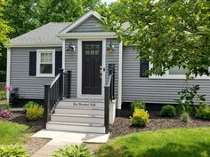 a small gray house with black shutters and steps leading up to the front door