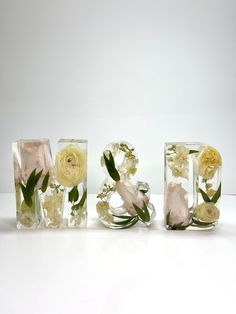 three glass blocks with flowers in them sitting on a table next to the letters love