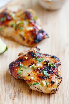 two pieces of grilled chicken on a cutting board next to a slice of lime