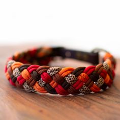 an orange, brown and white braided bracelet on top of a wooden table in front of a white wall