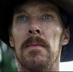 a close up of a person wearing a hat with blue eyes and a goatee