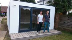 two men standing in front of a small white building with sliding glass doors on the outside