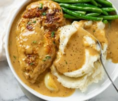 a white plate topped with mashed potatoes and meat covered in gravy next to green beans