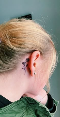 the back of a woman's head with a small flower tattoo on her left ear