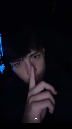 a man with his finger on his lips in the dark, looking at something off camera