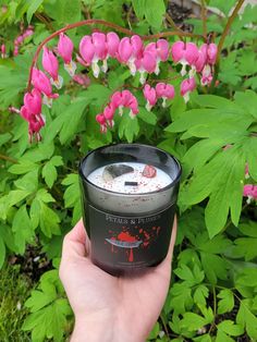 a hand holding a candle in front of pink flowers