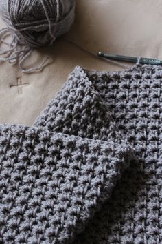 two gray crocheted squares next to a ball of yarn