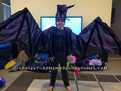 a person in a costume standing next to a tv with two dragon wings on it