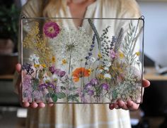 a woman holding up a glass box with flowers in it's front and back