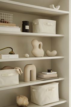 the shelves are filled with white containers and other items for storage, such as vases