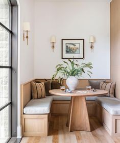 a corner table with two benches and a potted plant in the center is surrounded by wood paneling