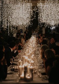 a long table with many lit candles and people sitting at the tables in front of them