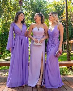 three women in long purple dresses standing on a wooden deck and smiling at each other