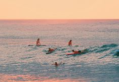 several people are surfing in the ocean at sunset