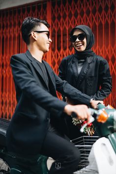 a man and woman riding on the back of a scooter in front of a red wall