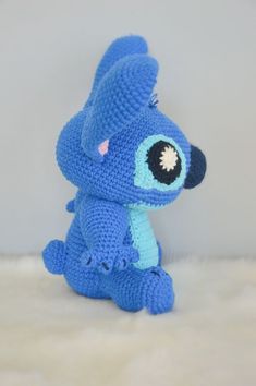 a blue crocheted stuffed animal sitting on top of a white rug next to a wall