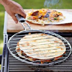 a person cooking food on top of a bbq with a pizza in the background