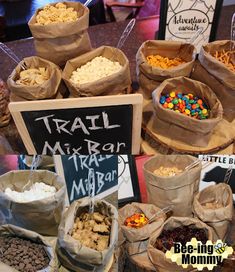 many bags full of different types of snacks on display at a market table with signs that say trail mix, trinki macaro and m & msap