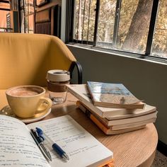 a cup of coffee, notebooks and pen on a table in front of a window